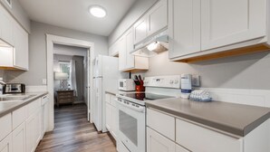 Una cocina moderna con armarios blancos, microondas, horno y una encimera con cafetera y utensilios.