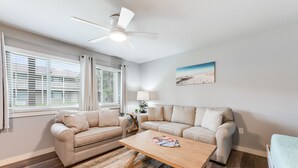 Una sala de estar con dos sofás color beige, una mesa de centro de madera, un ventilador de techo y un cuadro en la pared.