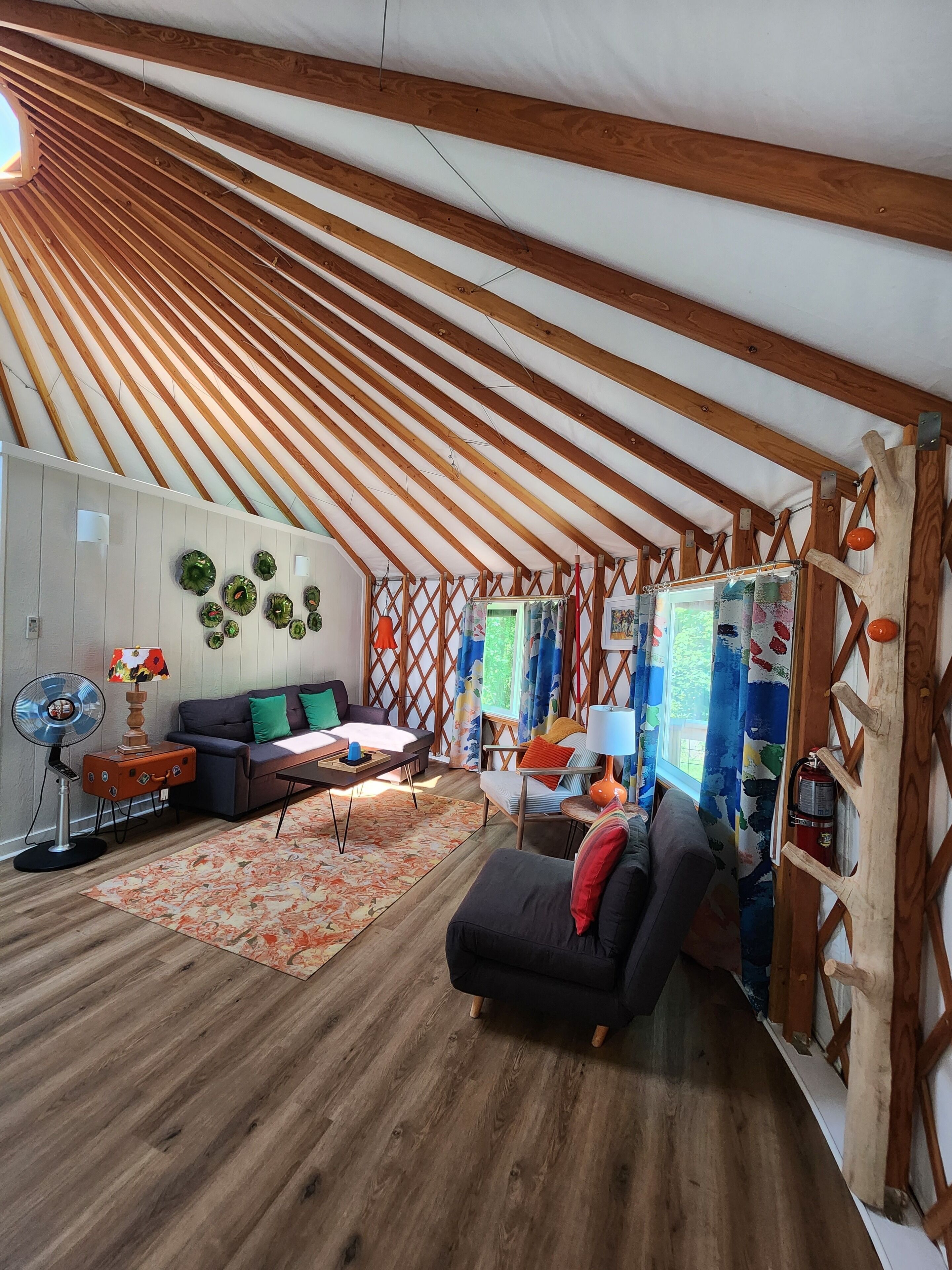 Una habitación tipo tienda acogedora y bien iluminada, con vigas de madera, un sofá, una mesita y un ventilador.
