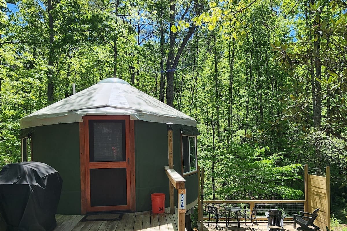 A small, single-story cabin with a porch, a covered grill area, and a deck with outdoor seating.