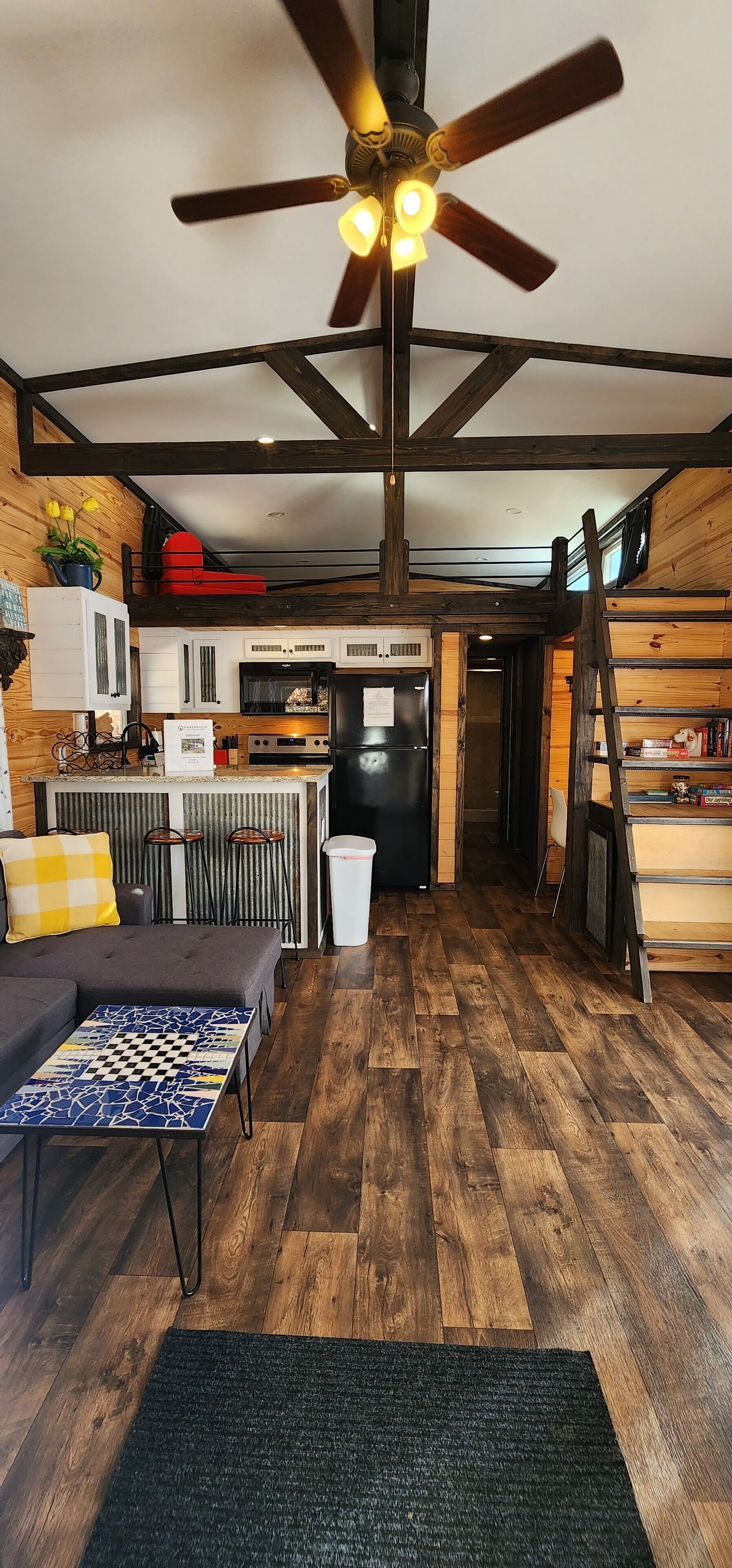 A compact kitchen with modern appliances, a dining area with a checkered table, and a ceiling fan.