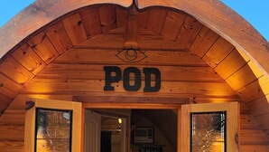 Puinen mökin sisäänkäynti, jonka yläpuolella on kyltti, jossa lukee: ”POD”.