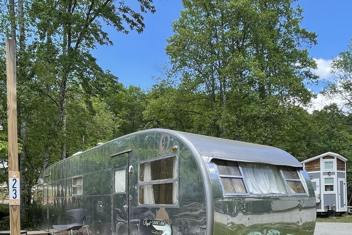 A vintage camper with a covered dining area, a small deck, and propane tanks.