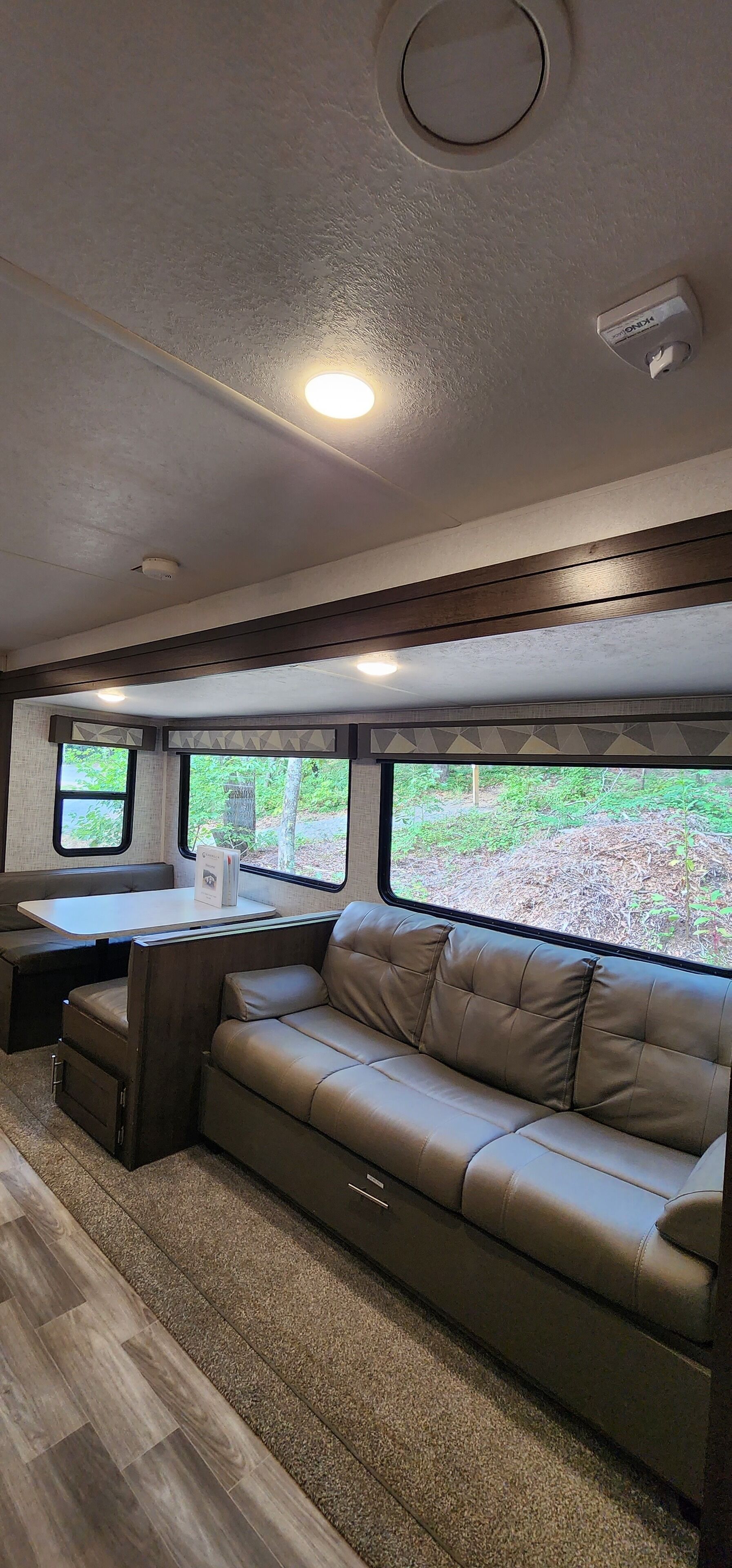 A cozy RV interior with a sofa, a table, and a window offering a view of greenery.