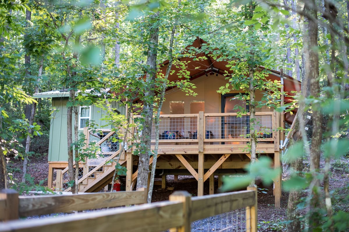 A wooden cabin with a deck and stairs, surrounded by trees.