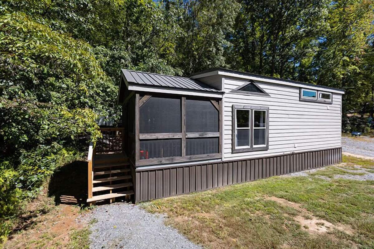 A mobile home with a covered porch, a small window, and a wooden deck.