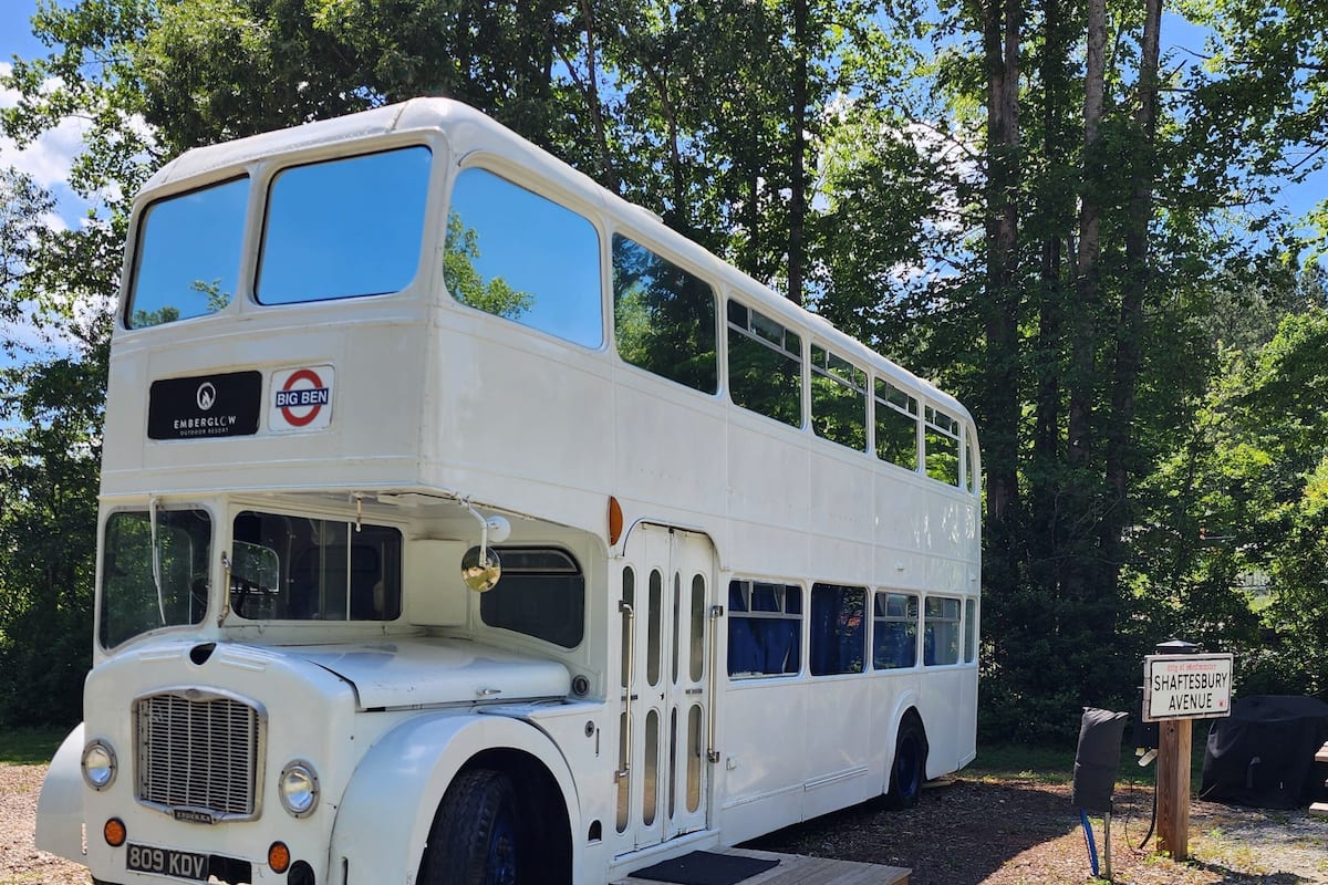 A white double-decker bus parked on a gravel path with a sign indicating 'Shaftesbury Avenue'.
