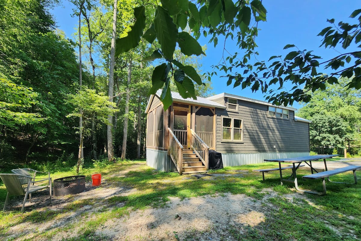 A small cabin with a porch, a picnic table, and a grill area.