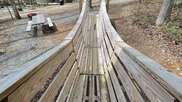 A wooden bench in a campground with picnic tables and cabins in the background.