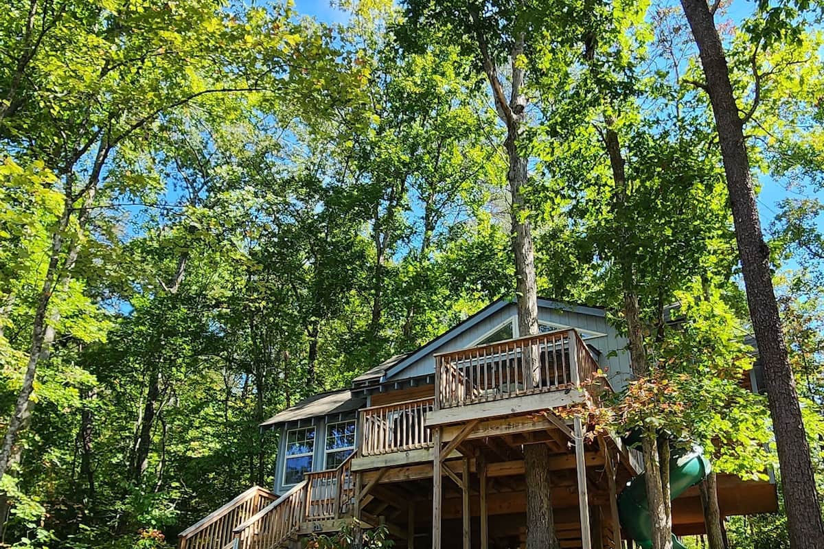 A wooden cabin with a deck and stairs, surrounded by trees.