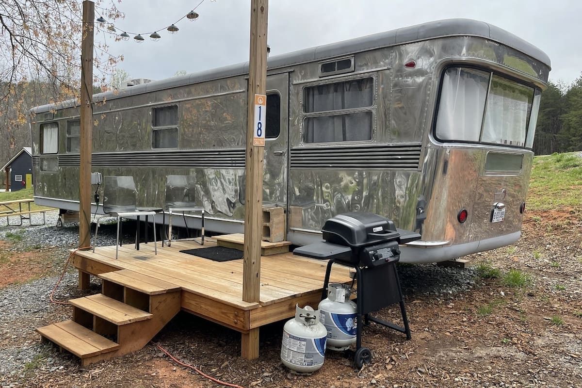 A stationary RV with a wooden deck, outdoor seating, and propane tanks.