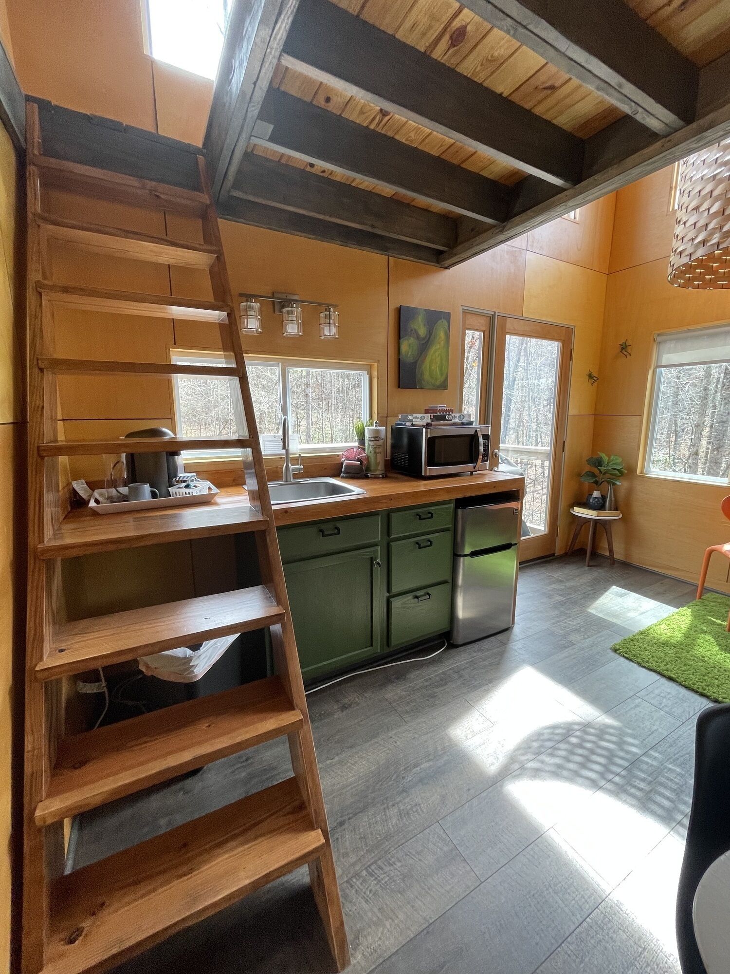 A kitchen with wooden beams, a built-in ladder, a microwave, and a sink.