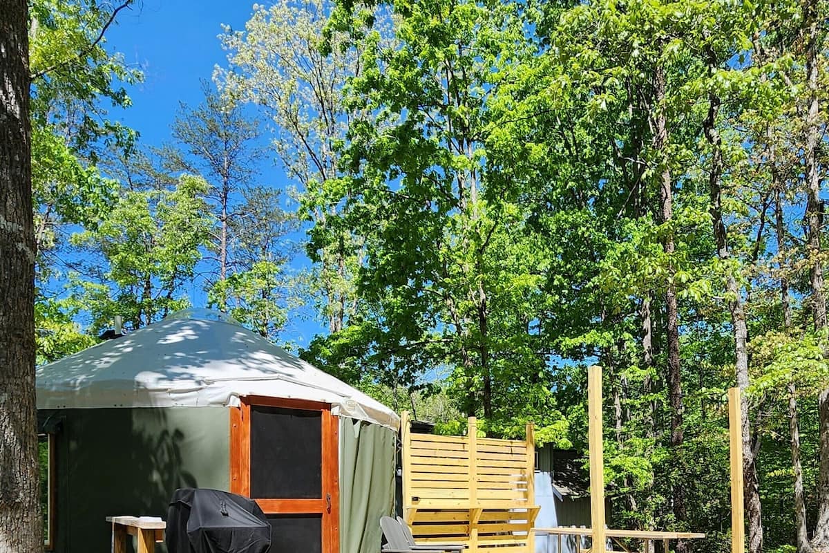 A small, single-room tent with a wooden deck and a covered grill area.