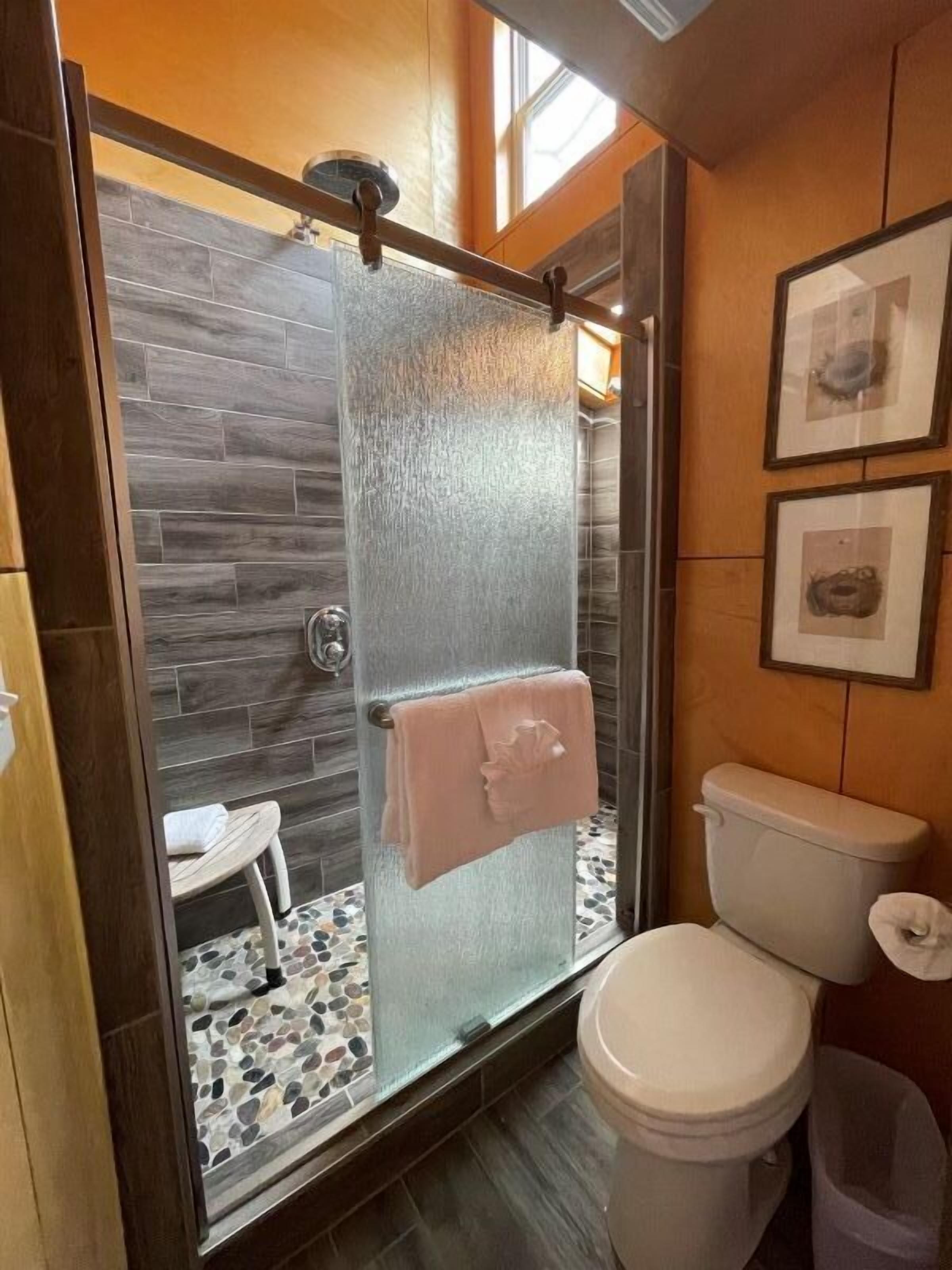 Un baño moderno con ducha envuelta en vidrio, inodoro blanco y una pequeña zona de estar.