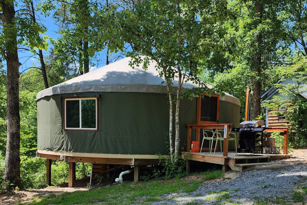 A small, green, dome-shaped tent-like structure with a window and a door, surrounded by trees.