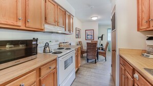 A kitchen with wooden cabinets, a microwave, stove, and a dining area with wicker chairs.