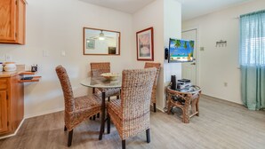 A dining area with wicker chairs, a glass table, and a television on a stand.