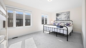 Een slaapkamer met een bed, ramen, een plafondlamp en een kunstwerk aan de muur.