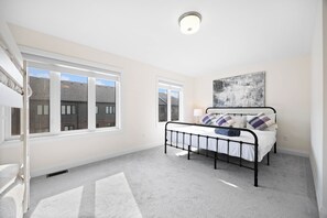 A bedroom with a bed, windows, a ceiling light, and a wall-mounted artwork.
