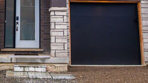 Een tweelaags huis met garage, voordeur en een groot raam op de bovenverdieping.