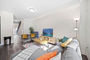 Un salon moderne avec un canapé, une table basse, un téléviseur et un escalier en arrière-plan.