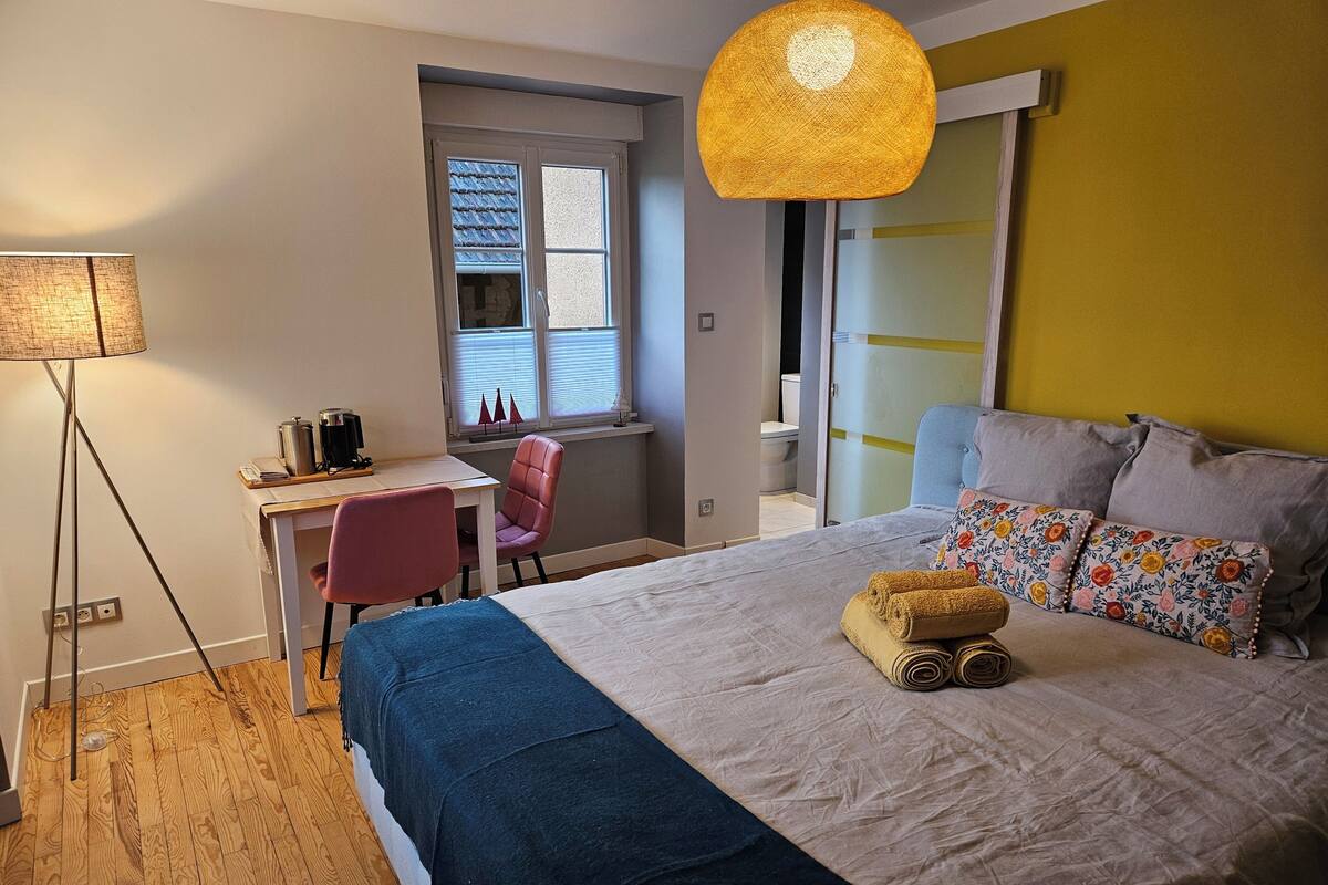 Un dormitorio con cama, escritorio, silla, lámpara y ventana.