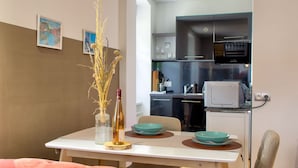 A dining area with a table set for two, a vase with dried plants, and a kitchen in the background with modern appliances.
