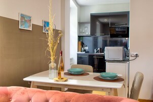 Un comedor con una mesa preparada para dos, un jarrón con plantas secas, y una cocina de fondo con electrodomésticos modernos.