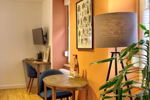 Una habitación acogedora con una mesa de madera, dos sillas, una impresión enmarcada de motivos botánicos, una lámpara y una planta.