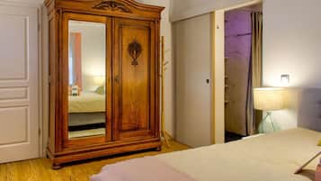 A bedroom with a wooden wardrobe, a bed with a white duvet, a bedside lamp, and a bathroom visible through an open door.