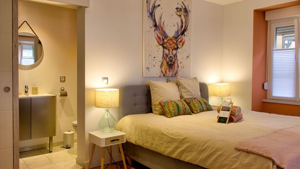 A bedroom with a bed, bedside lamps, a rug, a painting, and a window.