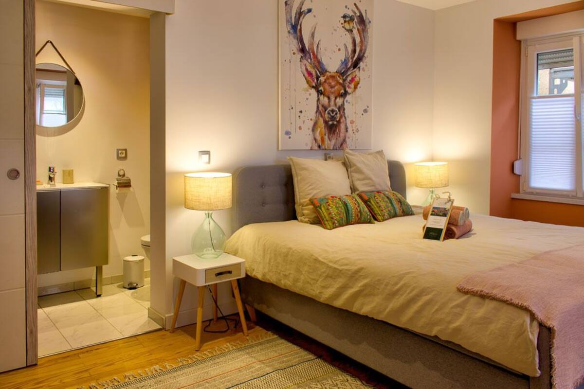 Un dormitorio con cama, lámparas de noche, una alfombra, un cuadro y una ventana.