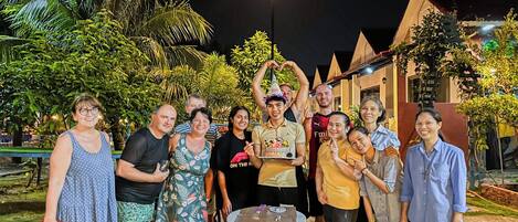 A group of people gathered around a table with food and drinks, outdoors at night.