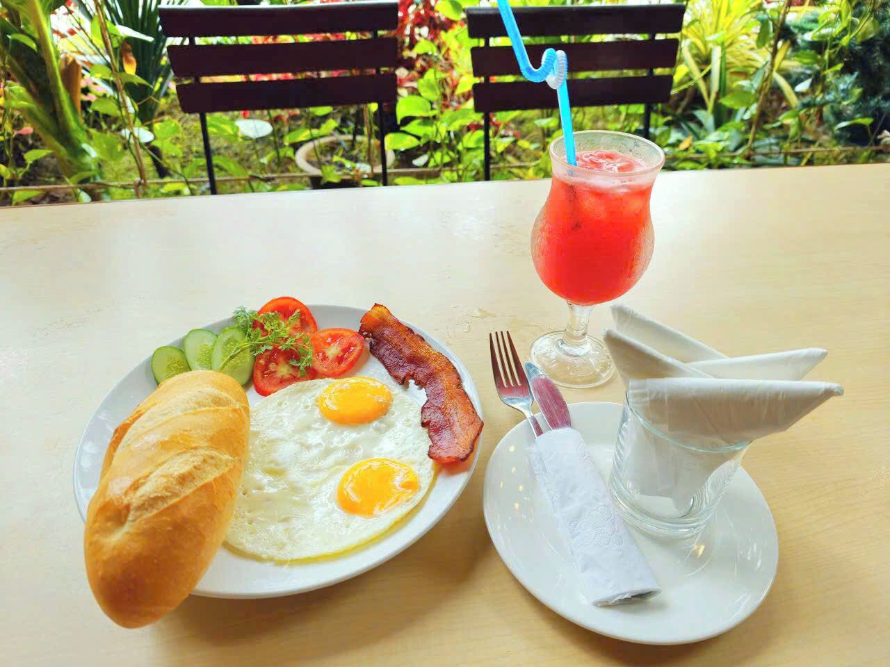 A breakfast plate with eggs, bacon, tomatoes, and a croissant, and a glass of red drink with a straw.