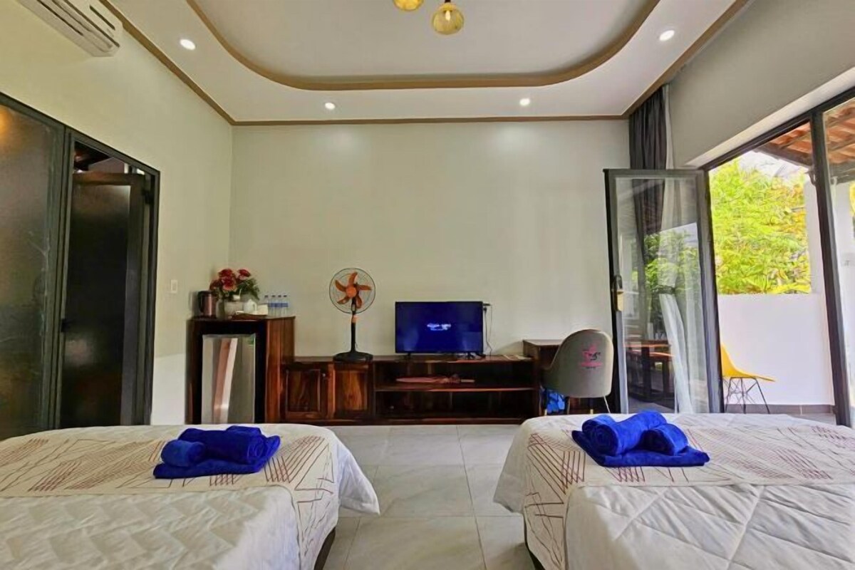 A hotel room with two beds, a TV, a desk, and a sliding glass door to the outside.