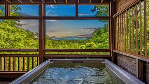 A hot tub with a view of a forested landscape through large windows. - Sevierville Cabin, Hot Tub & Mountain Views (Sevierville)