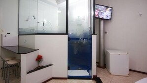 A modern bathroom with a glass shower enclosure, a small sink area, and a television mounted on the wall. - PRIME MOTEL AMERICANA (Americana)