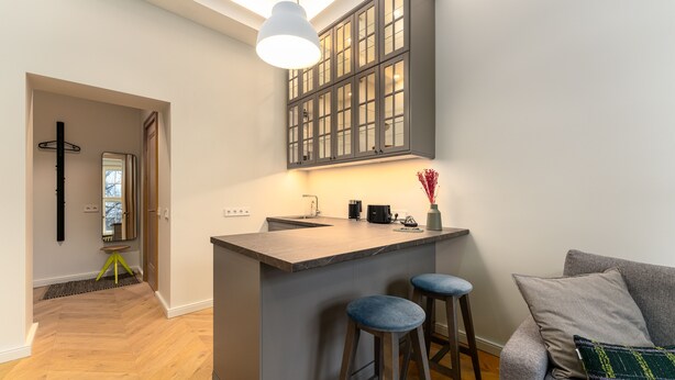 Een moderne keuken met een centraal eiland, barstoelen en een grijze bank met een decoratief kussen.