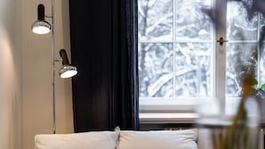Een kamer met een bed, een vloerlamp en een raam met uitzicht op besneeuwde bomen.