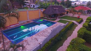 Una piscina con una struttura a tetto di paglia nelle vicinanze, circondata da siepi curate e un vialetto lastricato.