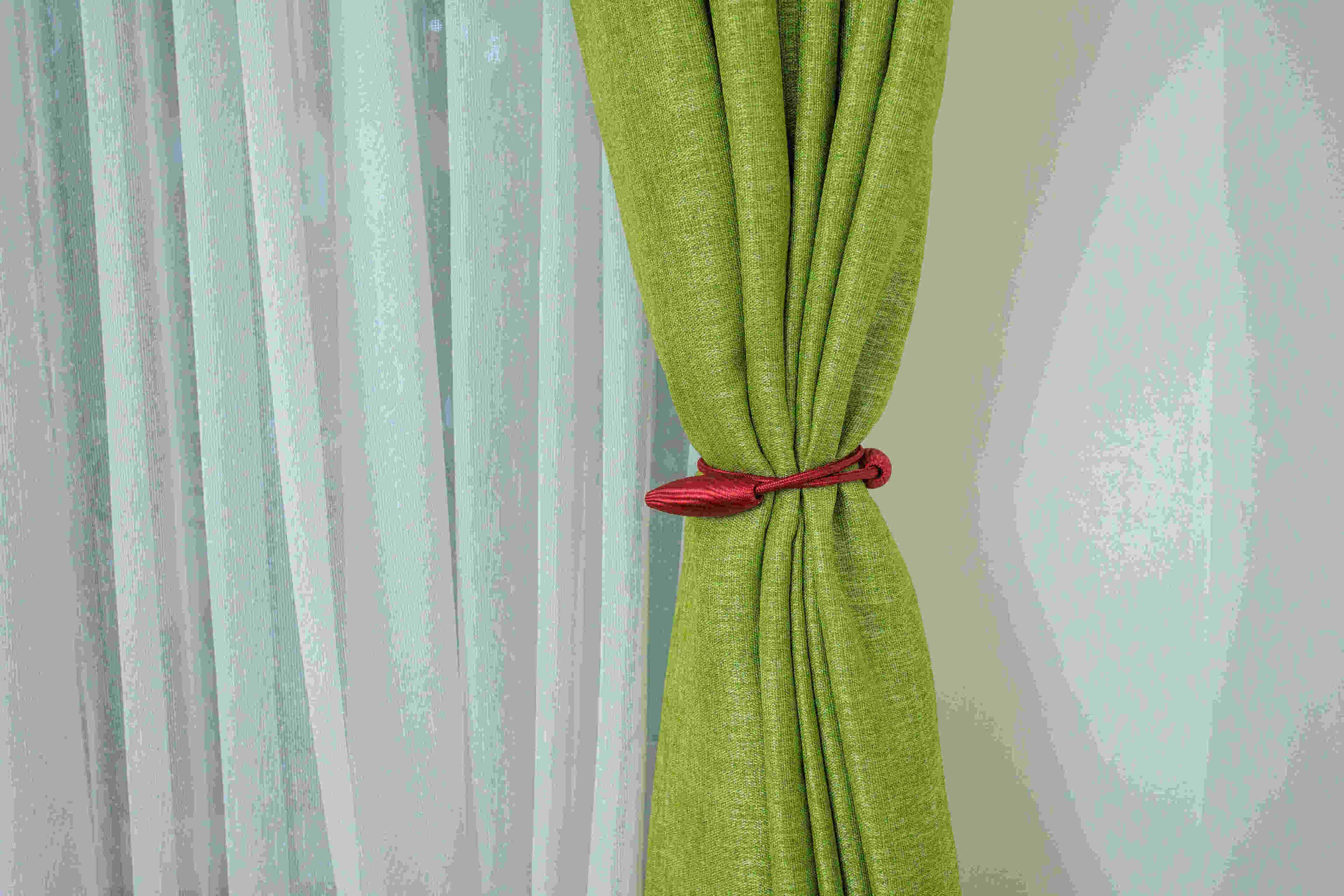 Un rideau vert, orné d’une pompon rouge, est accroché à un mur à la texture particulière.