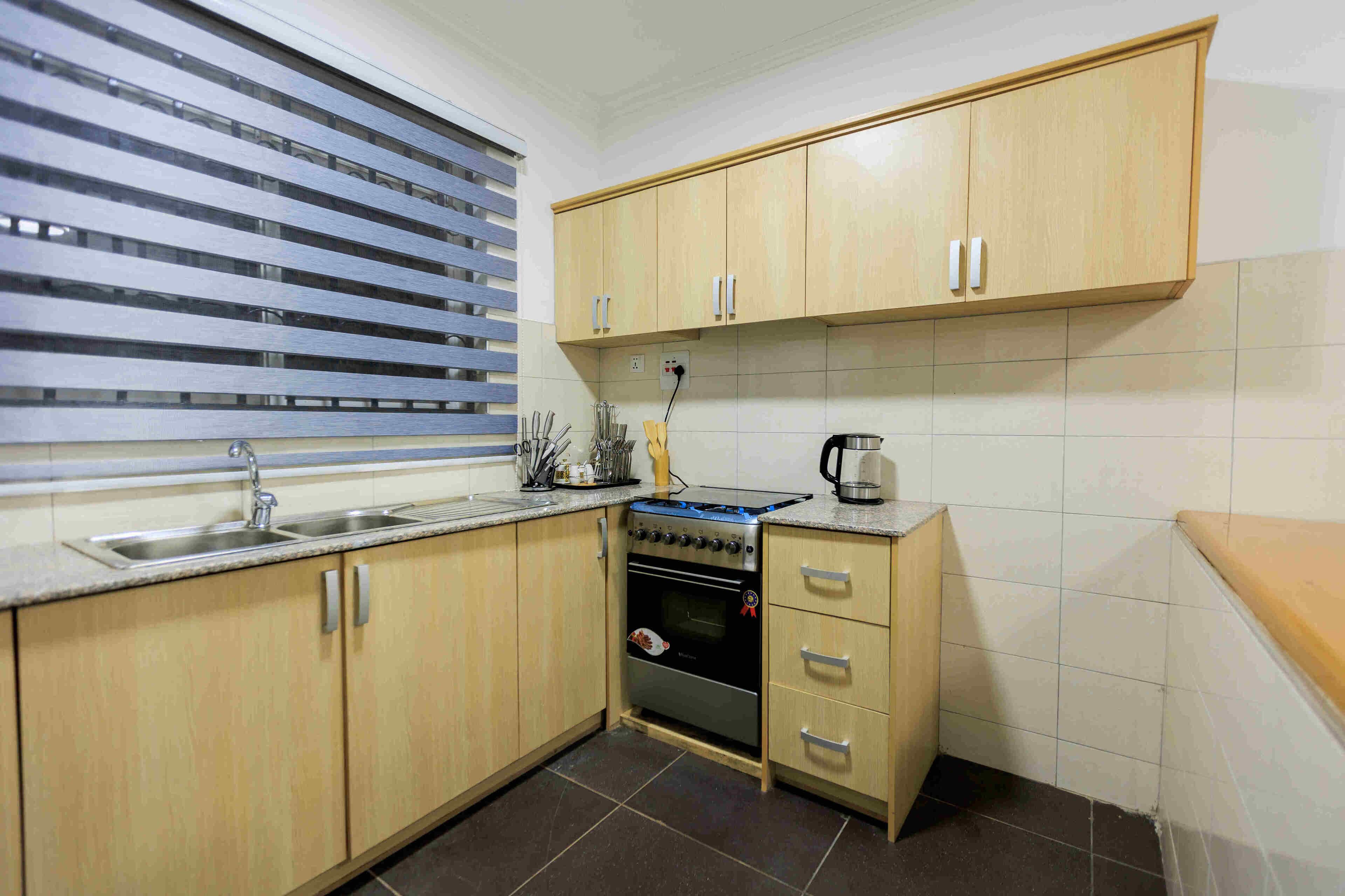 A kitchen with wooden cabinets, a gas stove, a sink, and a window with blinds.