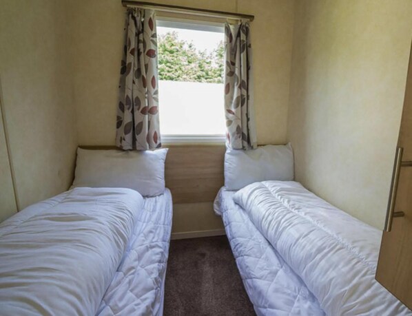 Een kleine, eenvoudige kamer met twee éénpersoonsbedden, een raam met gordijnen en een deur.
