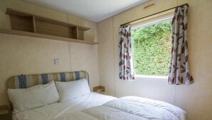 Um quarto com uma cama, uma cabeceira, uma janela com cortinas e uma prateleira sobre a cama.