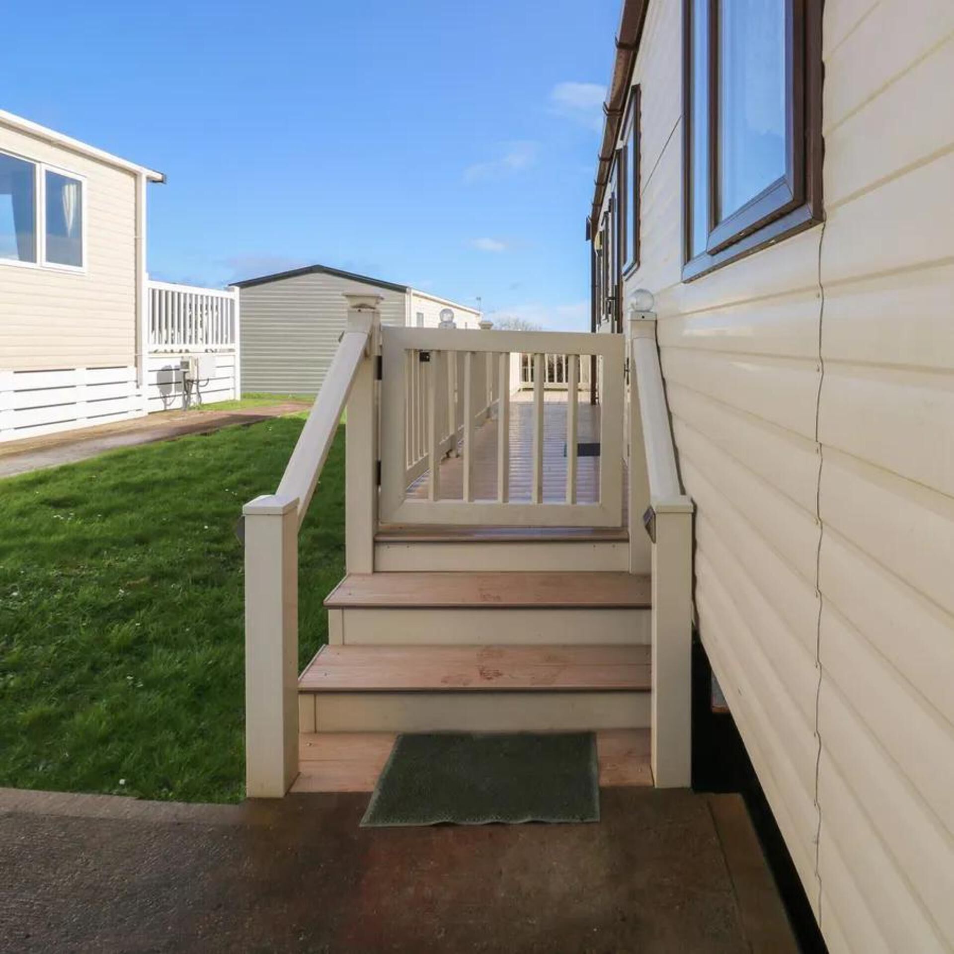 A set of wooden steps leading to a gated entrance of a mobile home with a clear sky in the background.