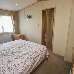 A bedroom with a bed, a bedside table, a wardrobe, and a door leading to another room. - Caravansleeps6-freeparking-quietretreat-nature (Paignton)