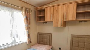 A compact bedroom with two beds, a window with curtains, and wooden cabinets above the beds.