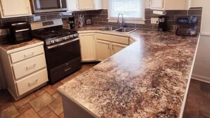 A modern kitchen with white cabinets, a granite countertop, a microwave, a stove, and a ceiling fan. - Our Home Away From Home! (Lansing)