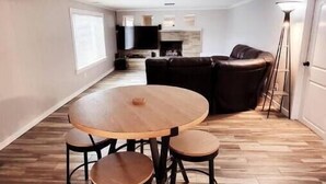 A spacious living area with a round wooden table and four stools, a dark leather sofa, and a fireplace. - Our Home Away From Home! (Lansing)