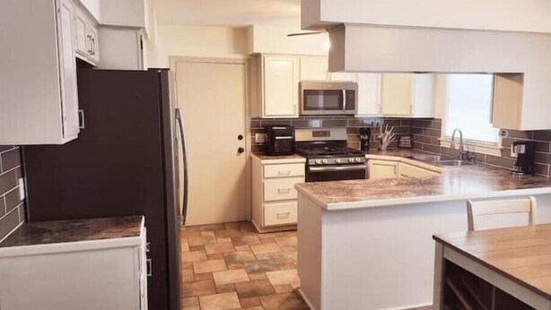 A modern kitchen with white cabinets, a black refrigerator, a microwave, a stove, and a sink. - Our Home Away From Home! (Lansing)